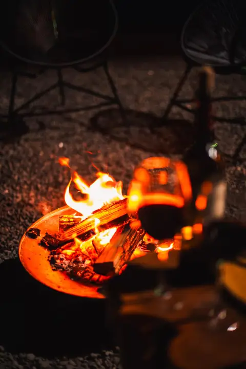 Fogo de chão aceso com taça de vinho ao lado, à noite